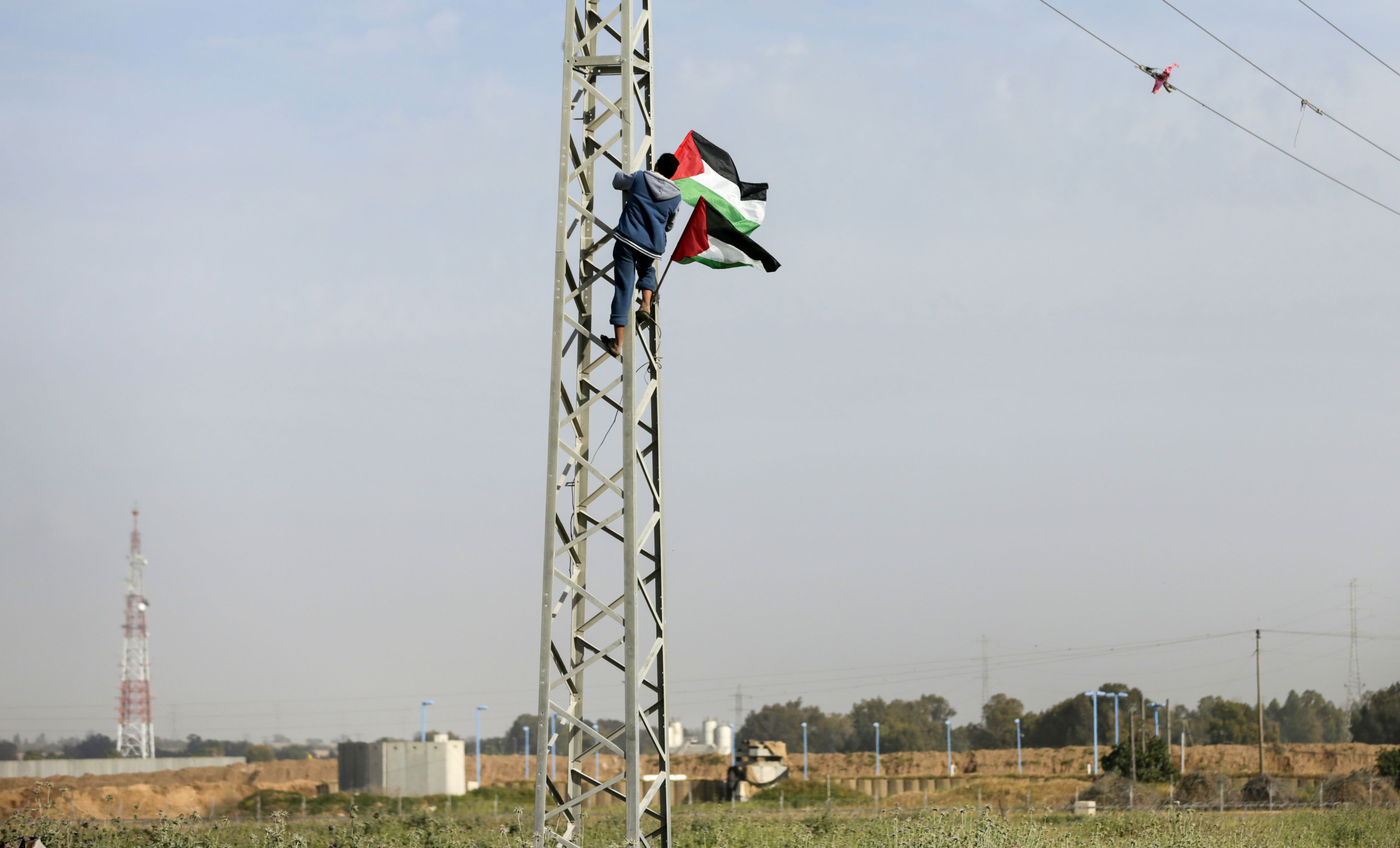 شاب يتسلّق عمود كهرباء قرب الحدود بين غزة، والمناطق المحتلة، ضمن تجهيزات مسيرة العودة