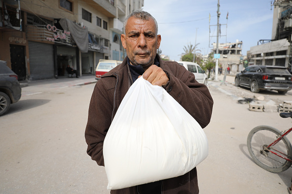 رجل في جباليا شمال قطاع غزة، يعرض كميّة طحين حصل عليها من أونروا مع دخول أول قافلة مساعدات إنسانية منذ أشهر (داوود أبو الكاس/getty). 