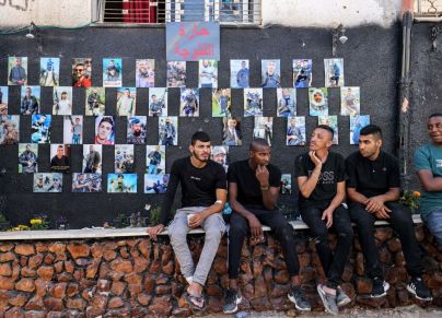 شبّان يجلسون أمام جدارية عليها صور لشهداء ارتقوا برصاص إسرائيلي في مخيم جنين -  AHMAD GHARABLI/Getty