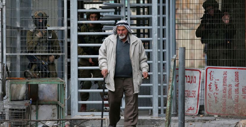 صورة إرشيفية لفلسطيني مسن يعبر من نقطة تفتيش بينما يقف جنود الاحتلال. تصوير حازم بدر 